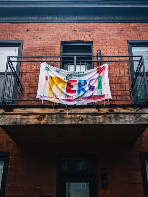 Balcon avec drapeau peinturé à la main multicolore disant merçi par Muneeb Syed.